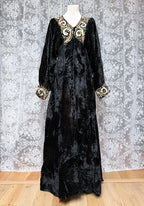 Black velvet dress with gold embroidery on a mannequin against a floral wallpaper background.