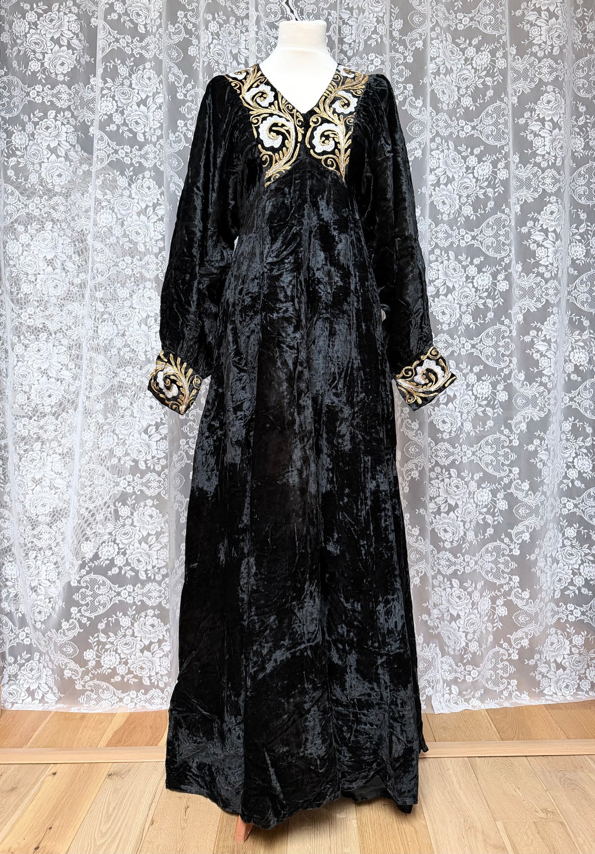 Black velvet dress with gold embroidery on a mannequin against a floral wallpaper background.